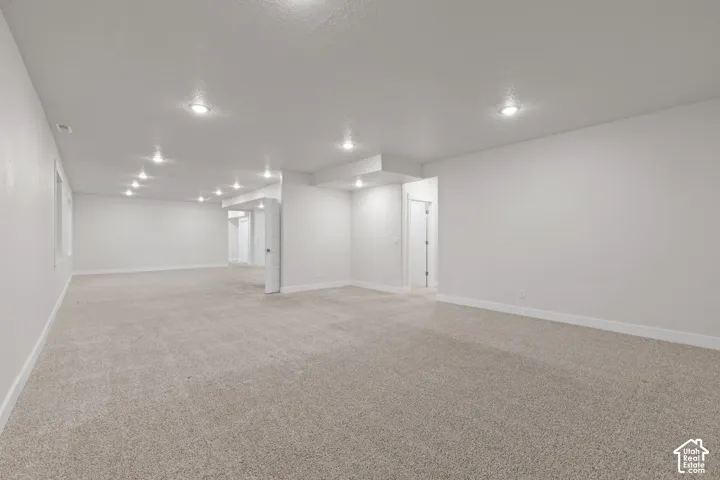 Expansive open-concept room featuring neutral-toned carpeting, recessed lighting, and crisp white walls