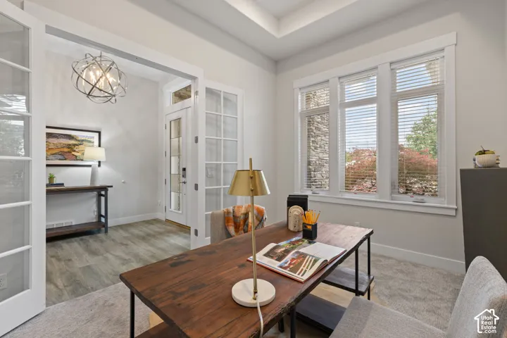 French doors with glass panels open to a room featuring a large multi-pane window, carpet flooring, and a tray ceiling