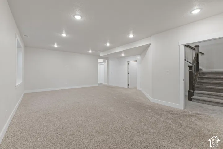 Spacious room with plush carpeting, recessed lighting, white walls, and a window