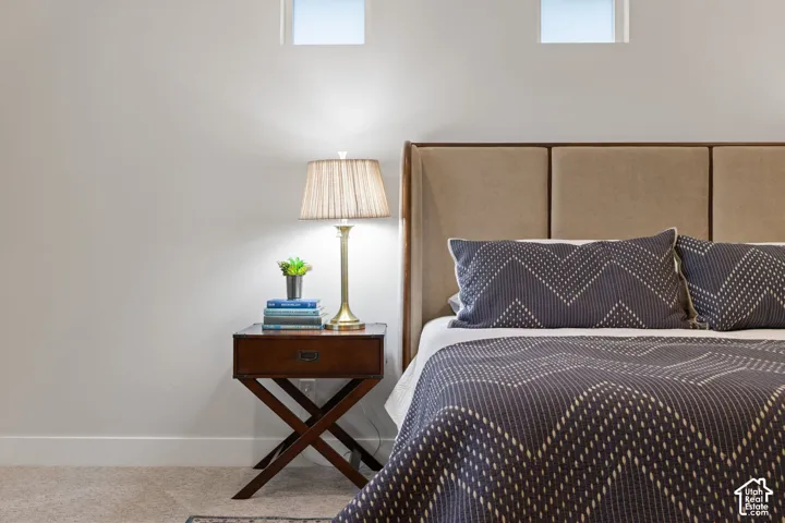Upholstered headboard with panel detailing, carpeted flooring, and high-set windows