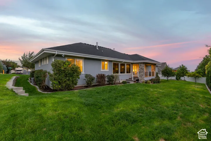 Manicured lawn, mature landscaping, stone facade accents, large windows, and an elevated deck