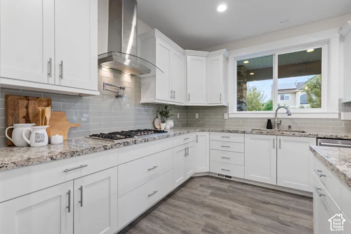 White shaker-style cabinetry, stainless steel appliances, light-toned tile backsplash, and wood-finish flooring