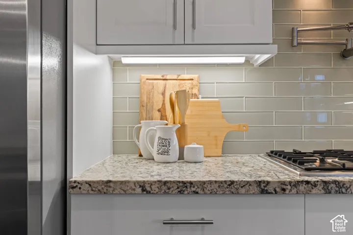 Stainless steel refrigerator and range, shaker-style upper cabinetry, undermount cabinet lighting, tile backsplash, and speckled countertop