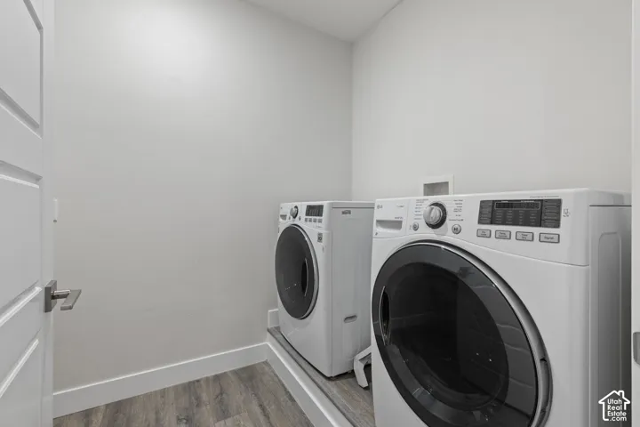 Dedicated laundry area featuring front-loading appliances, wood-finish flooring, and crisp white walls