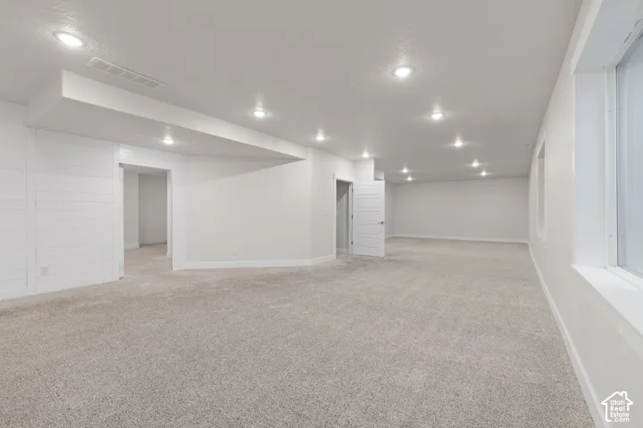 Expansive carpeted area with recessed lighting, white walls, and multiple windows