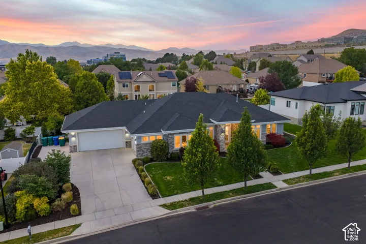 Elegant single-story residence showcasing a dark asphalt roof, attached two-car garage with concrete driveway, and manicured front landscaping featuring columnar evergreens and mature shade trees
