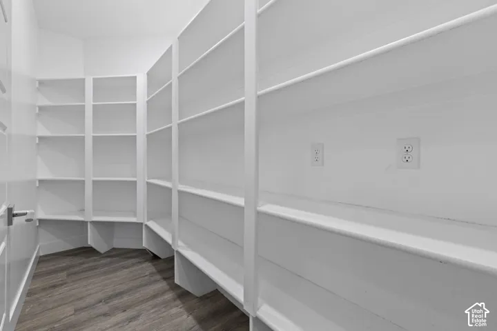 Generous walk-in closet featuring extensive built-in shelving and storage with white painted cabinetry, wood-finish flooring, and recessed electrical outlets for convenient organization and accessibility