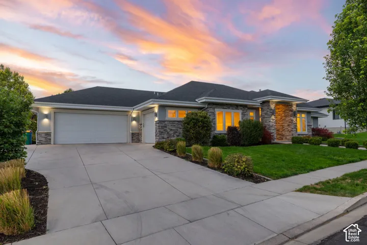 Stone and stucco exterior, dark shingle roof, two-car garage, concrete driveway, and established landscaping