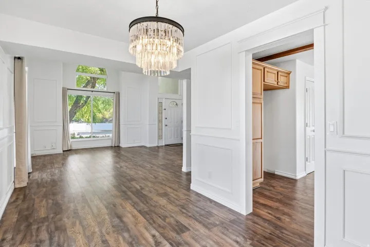 Wood-finish flooring, white paneled walls, and a multi-tiered crystal chandelier