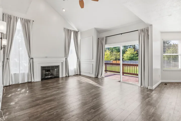 Vaulted ceilings, a fireplace with a white mantel, wood-finish flooring, and a sliding glass door to an outdoor deck