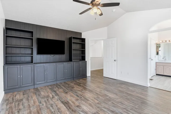 Built-in media center with shelving, wood-finish flooring, vaulted ceiling, and ceiling fan