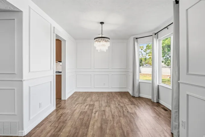Wood-finish flooring, accent wall paneling, and a tiered chandelier
