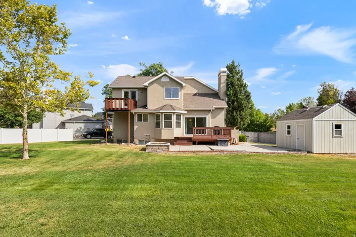 Expansive lawn with a wooden deck, second-story balcony, and a detached shed