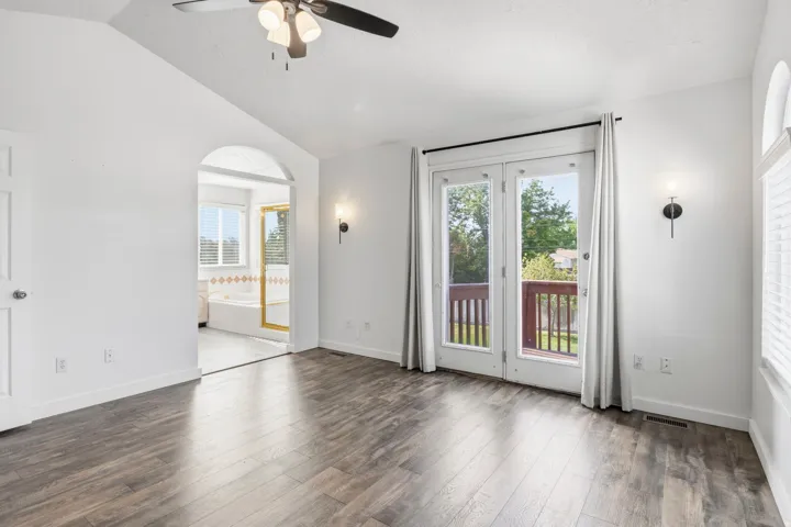 Wood-finish flooring, vaulted ceiling, ceiling fan, arched doorway, and French doors leading to a private deck