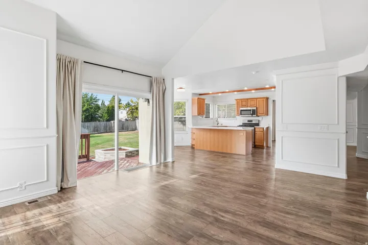 Wood-finish flooring, accent wall paneling, vaulted ceiling, sliding glass door to exterior, and a built-in kitchen island with white countertops