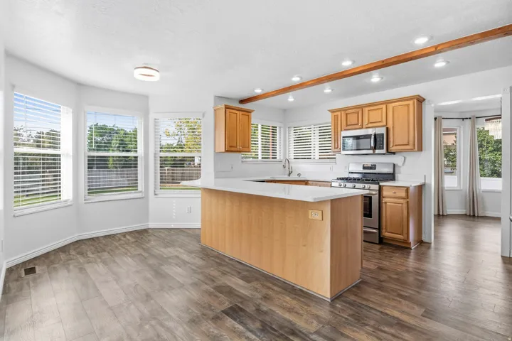 Kitchen featuring wood-finish flooring, light wood cabinetry, stainless steel appliances, a center island with a white countertop, and exposed wood beams