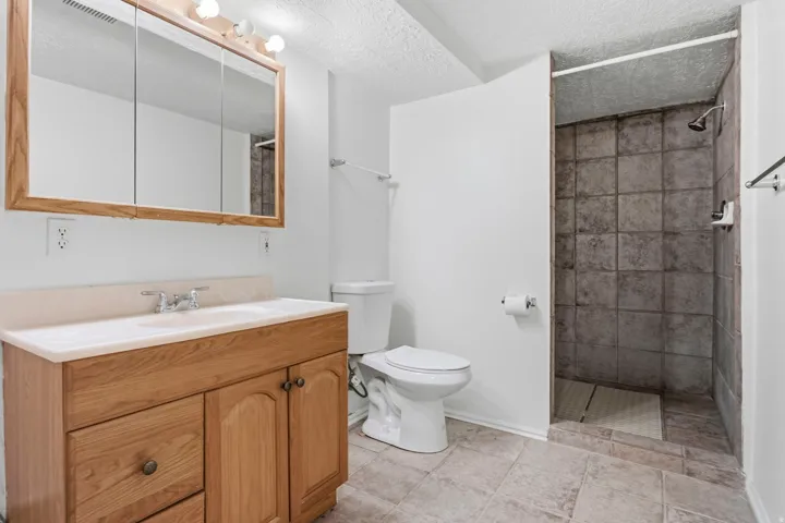 Bathroom featuring a wood-finish vanity with an integrated sink, a built-in medicine cabinet, and a tiled shower stall with a rain showerhead