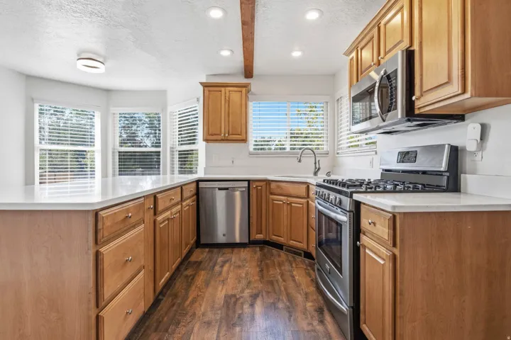 Kitchen featuring wood-finish flooring, light wood cabinetry, white countertops, and stainless steel appliances