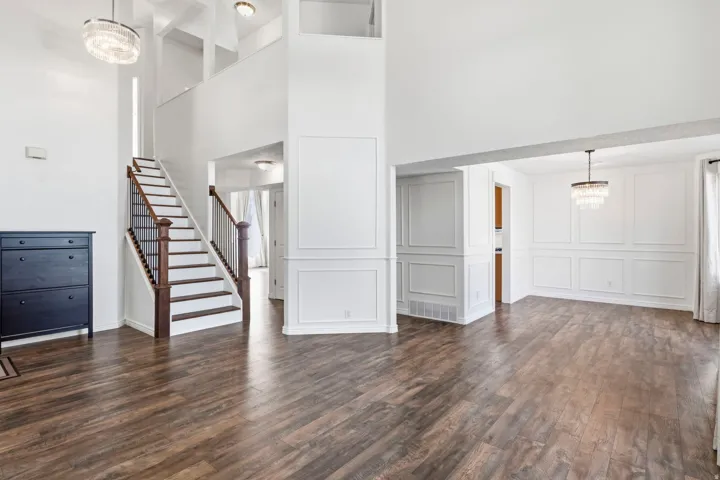 Wood-finish flooring throughout, bright white walls, decorative wall paneling, and two-story ceilings