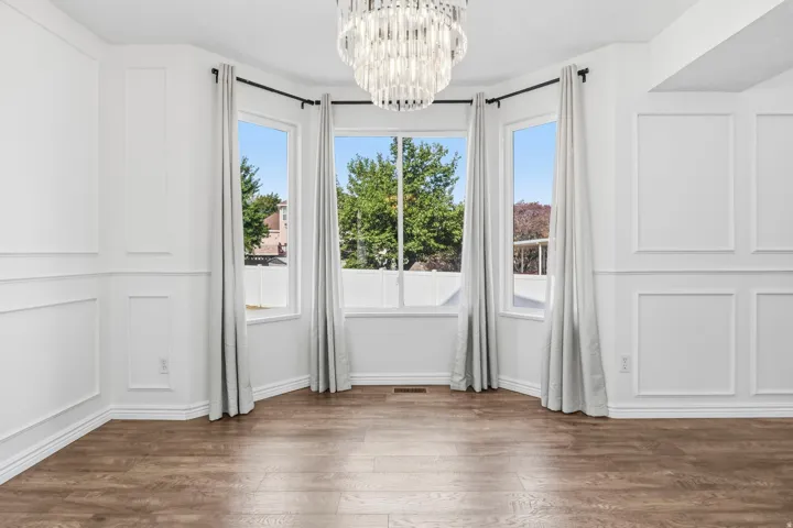 Bay window with multiple panes, wood-finish flooring, decorative wall paneling, and a contemporary chandelier