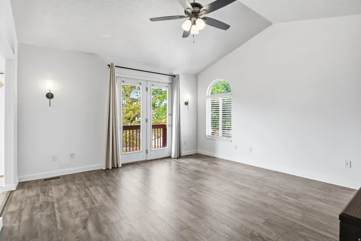 Vaulted ceilings with a ceiling fan, wood-finish flooring, and French doors leading to an exterior balcony