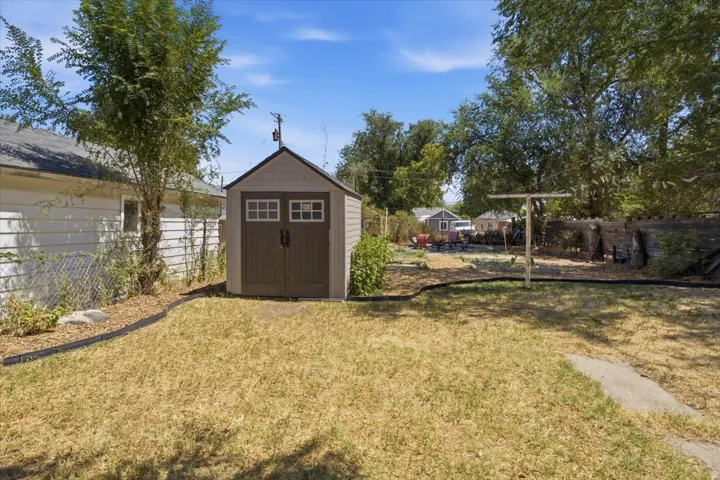 Spacious backyard with a storage shed featuring panel doors and transom windows, mature perimeter trees, and a defined planting area with edging
