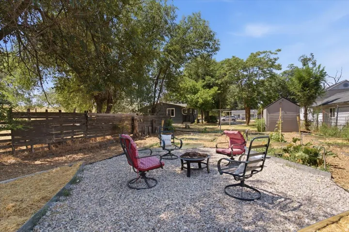 Gravel patio area, privacy fencing, mature trees, garden beds, and storage shed