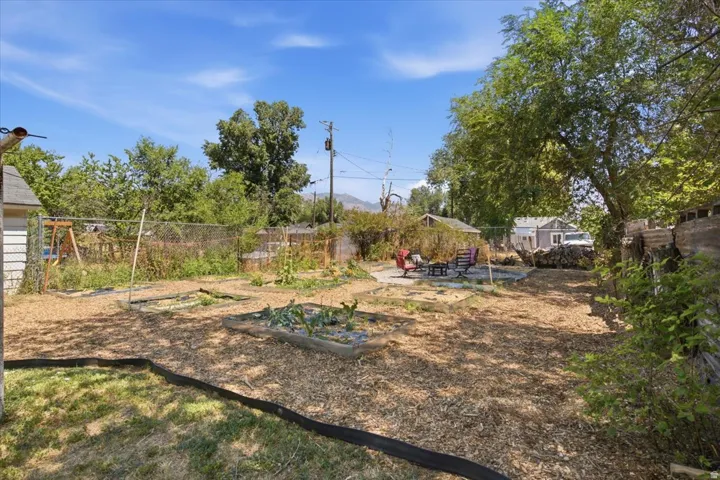 Expansive yard featuring wood chip ground cover, raised garden beds, and a chain-link fence
