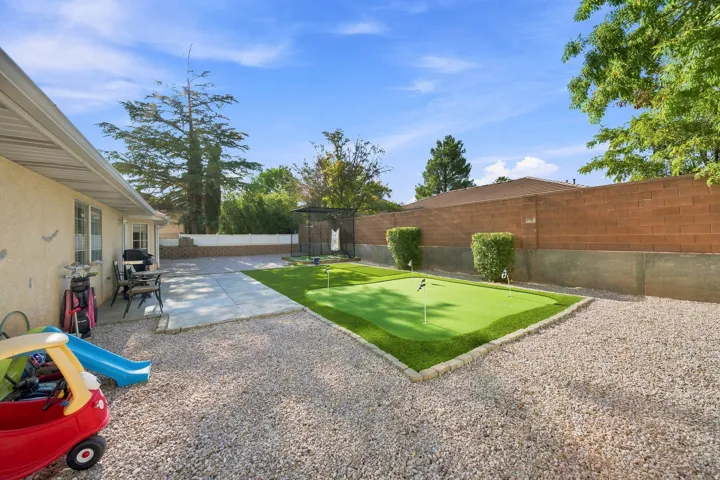 Expansive backyard featuring a putting green, gravel landscaping, a concrete patio, and a brick privacy wall