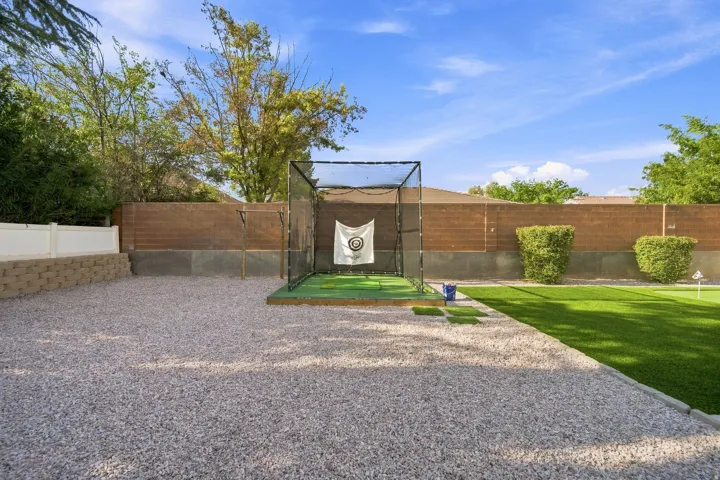 Expansive backyard featuring a gravel patio, synthetic turf lawn, and a golf practice enclosure