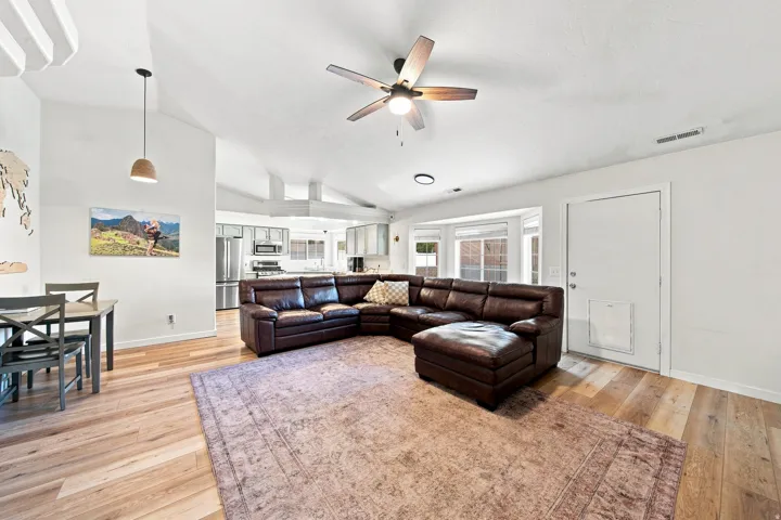 Vaulted ceilings with exposed beams, wood-finish flooring, kitchen with stainless steel appliances, bay window, and ceiling fan