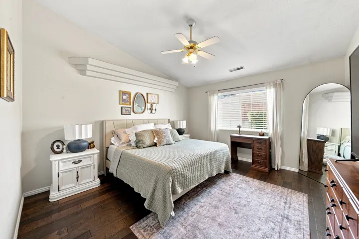 Vaulted ceiling with decorative beams, wood-finish flooring, ceiling fan with integrated lighting, window with blinds, and white curtains