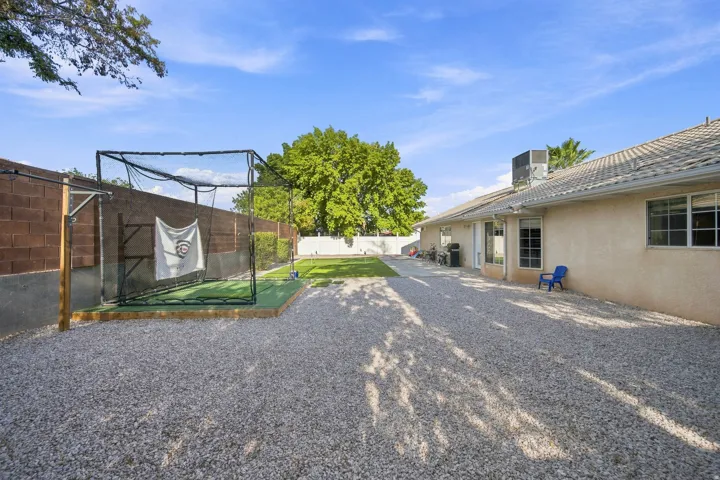 Expansive backyard with gravel and artificial turf areas, a permanent hitting cage, stucco exterior, and multi-pane windows