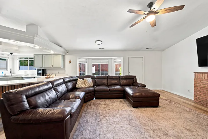 Open-concept living area featuring wood-finish flooring, a ceiling fan, and a brick-clad fireplace