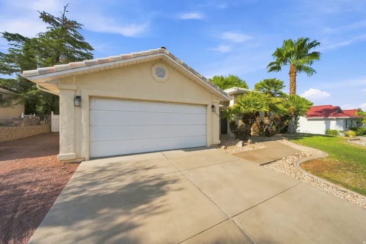 Two-car garage with a panel door, concrete driveway, stucco exterior, and a tile roof