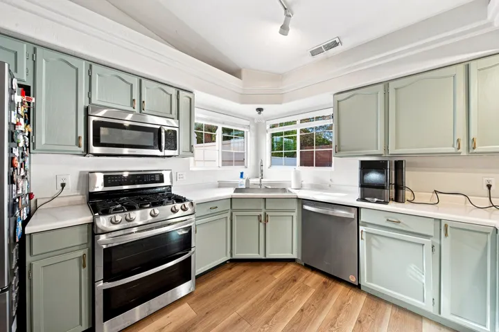 Kitchen featuring wood-finish flooring, light-toned cabinetry, stainless steel appliances, white countertops, and a window above the sink