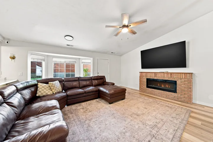 Bright living space featuring wood-finish flooring, a contemporary ceiling fan, and a brick-clad fireplace with an integrated linear insert