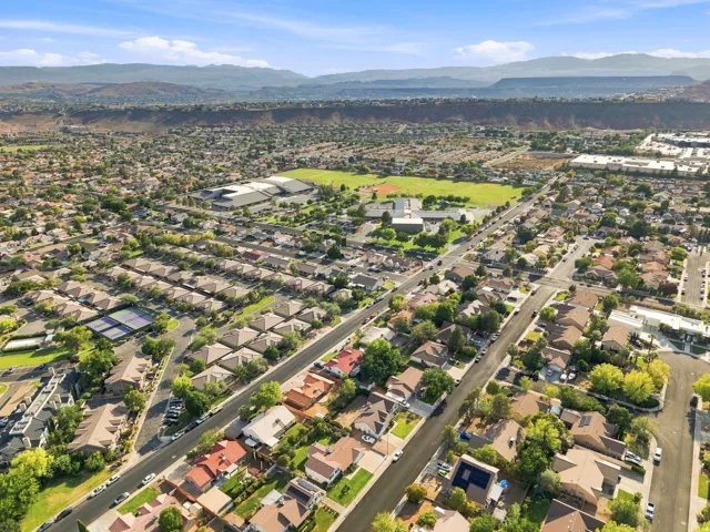 Aerial perspective showcasing residential streets, a large green playing field, and mountainous terrain in the distance