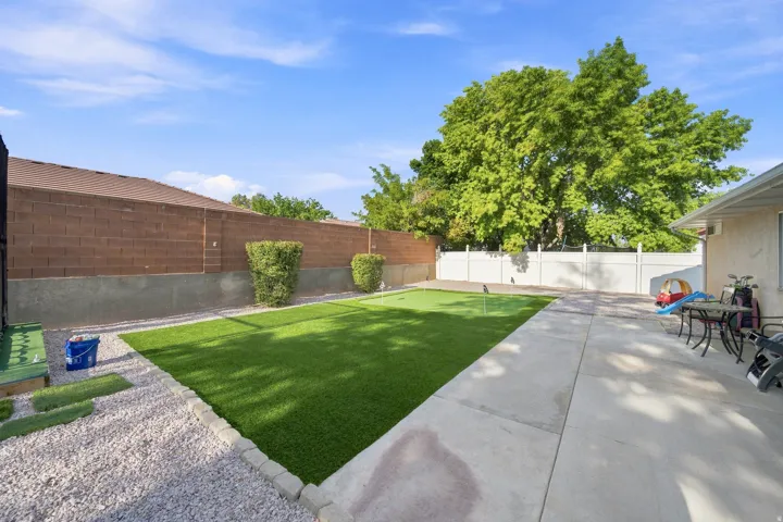 Spacious backyard featuring a putting green, concrete patio, gravel border, and a block fence