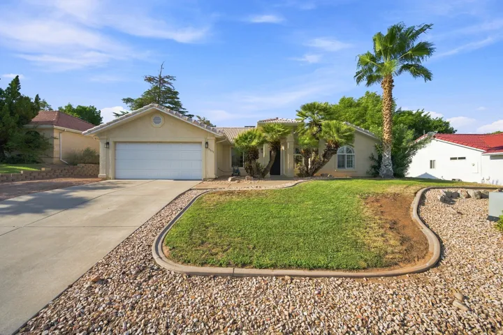 Single-story stucco exterior with an attached garage, concrete driveway, and established landscaping featuring palm trees and a partial lawn