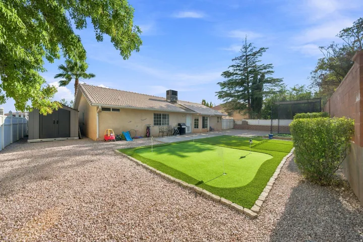 Expansive backyard featuring a putting green, gravel landscaping, and a permanent storage shed