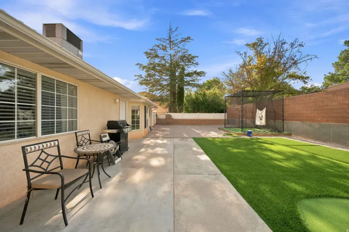 Expansive concrete patio with stucco exterior, multiple windows, artificial turf, and a putting green
