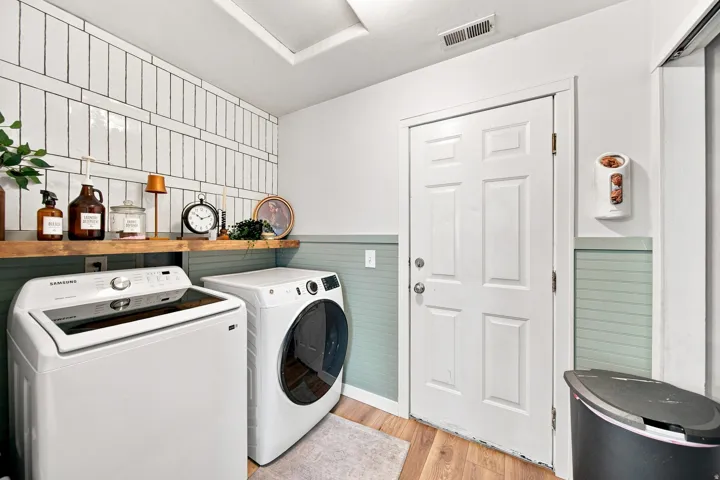 Laundry area featuring wood-finish flooring, half-wall paneling, and an exposed wood shelf