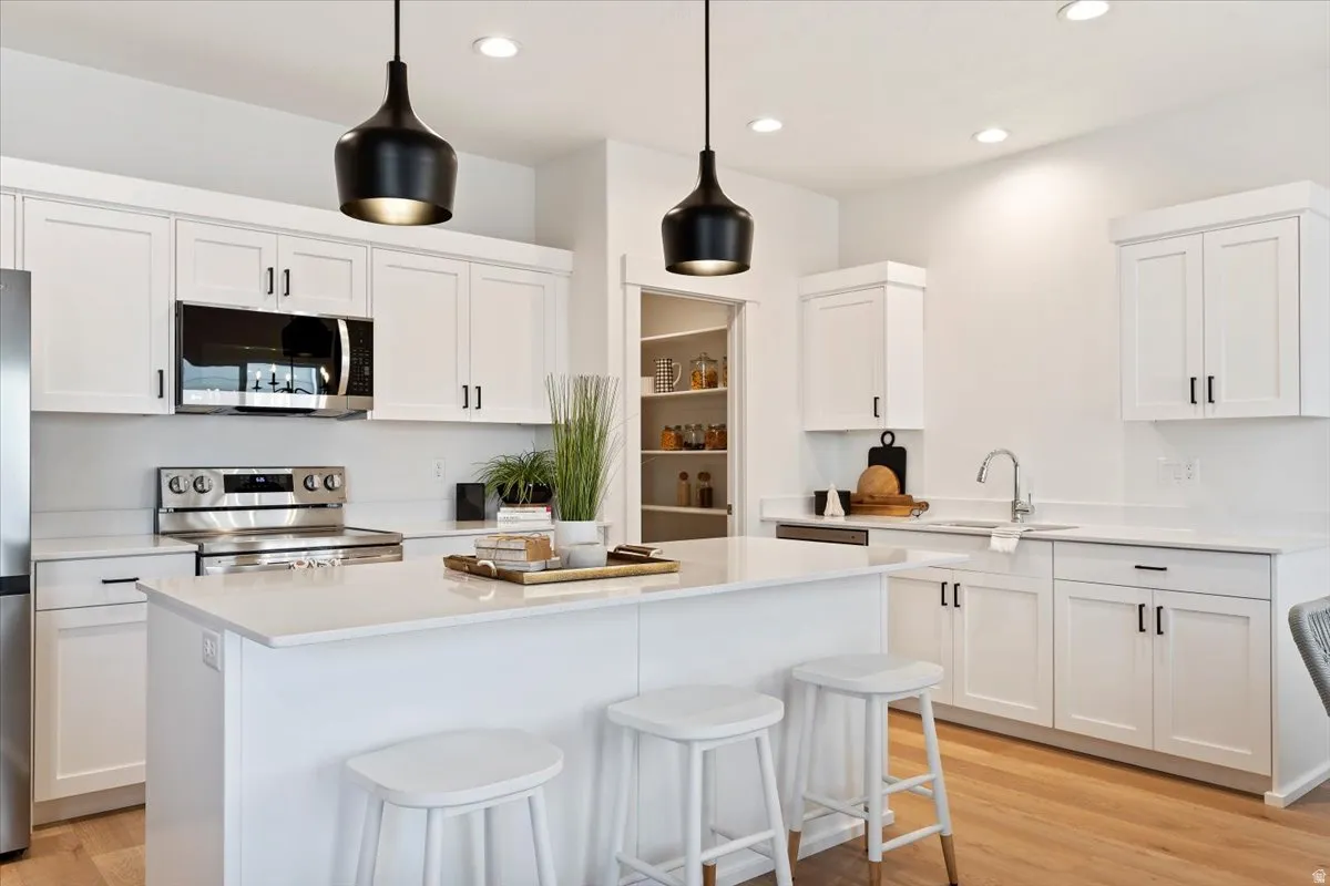 White cabinetry with black hardware, stainless steel appliances, central island with seating, recessed lighting, and wood-finish flooring