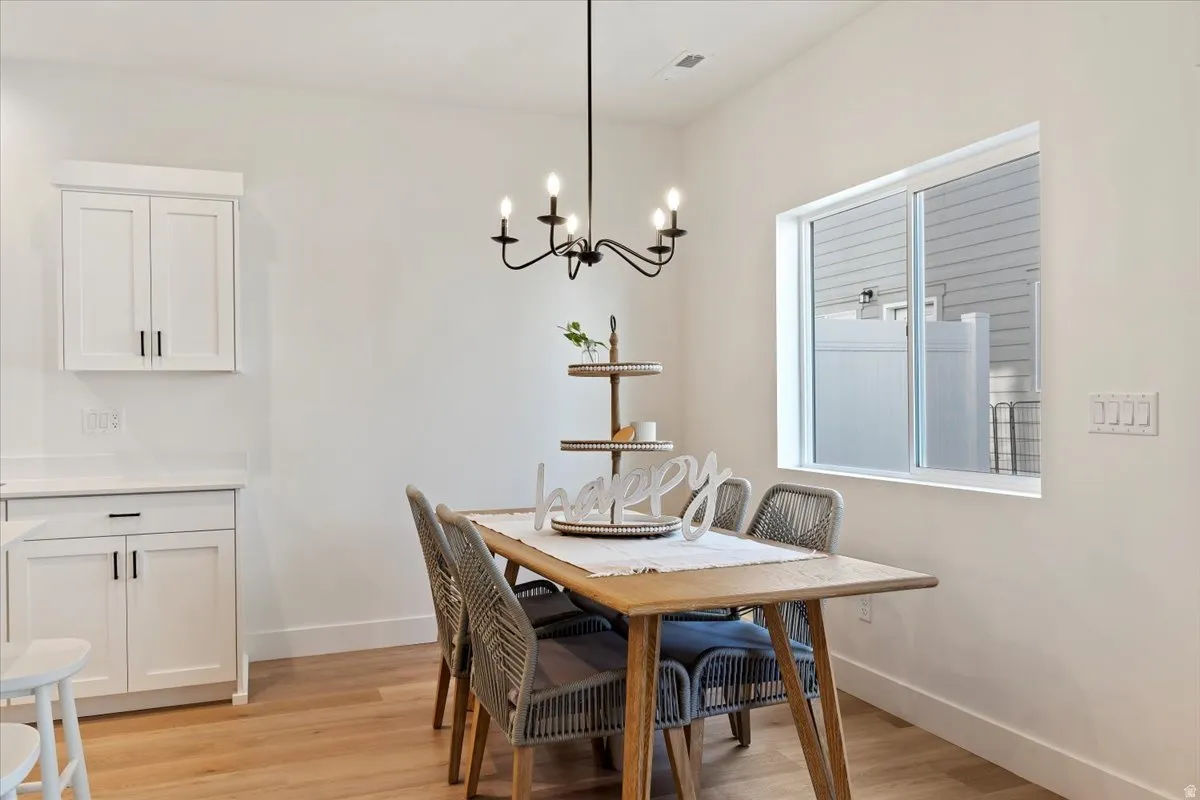 White cabinetry with dark hardware, a recessed window, a vaulted ceiling, wood-finish flooring, and a black metal chandelier