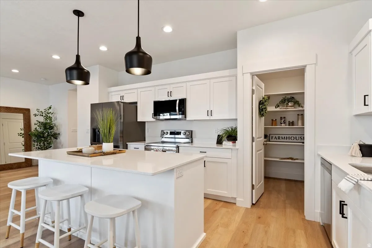 Modern kitchen featuring an island with white countertop, white cabinetry with dark hardware, stainless steel appliances, and wood-finish flooring