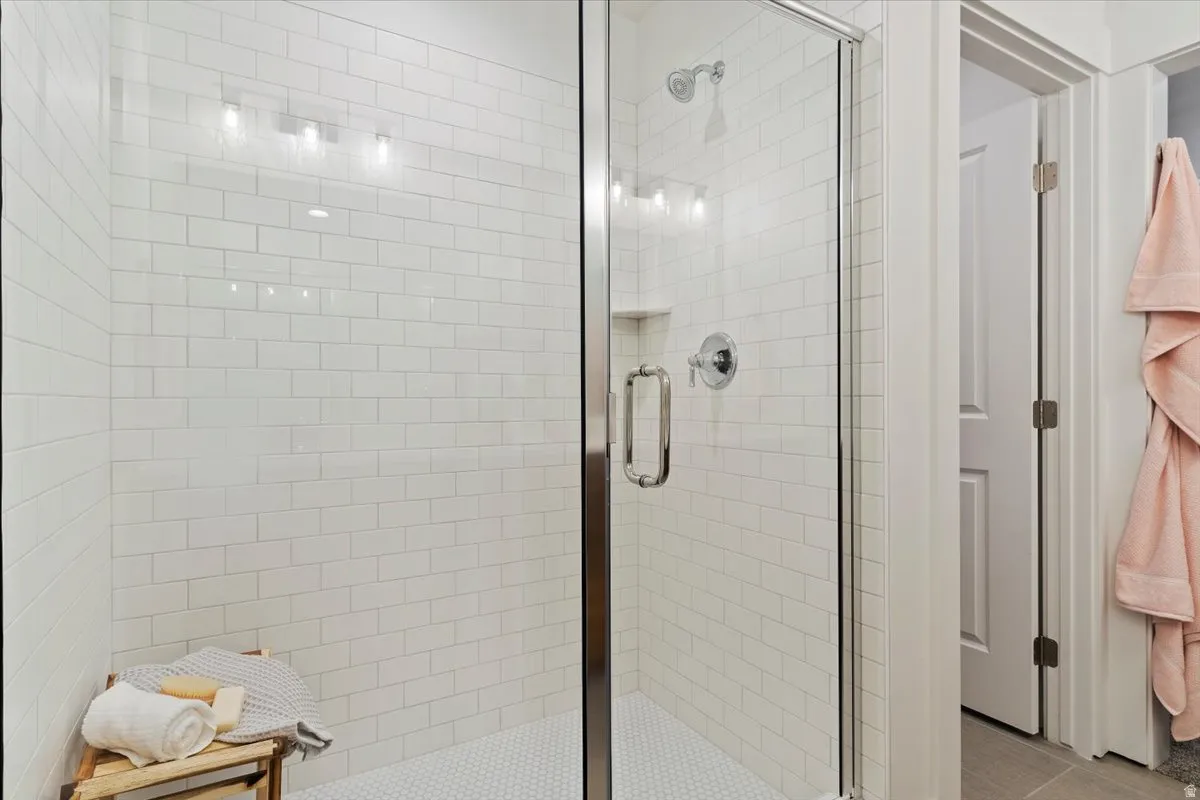 Shower enclosure with clear glass door, subway tile surround, hexagon tile flooring, built-in recessed shelf, and chrome fixtures