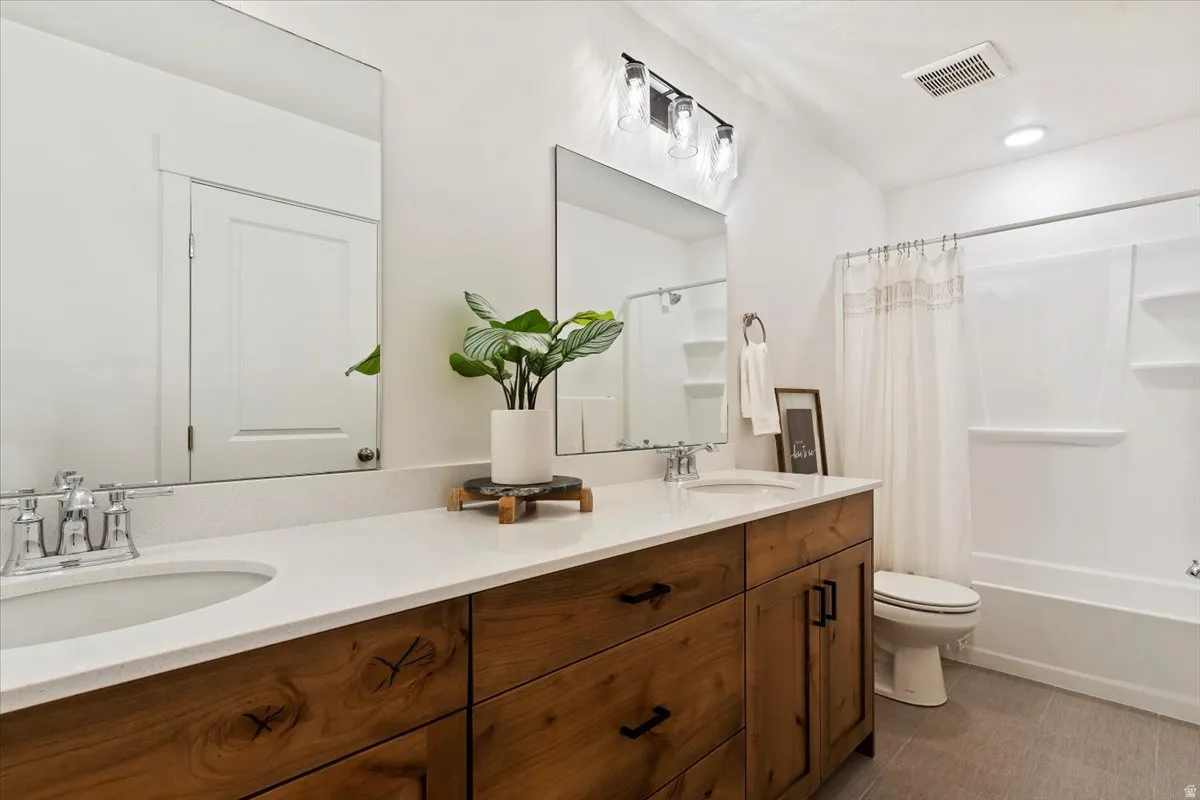 Double vanity with integrated sinks, wood-finish cabinetry, a white countertop, and a built-in bathtub with shower