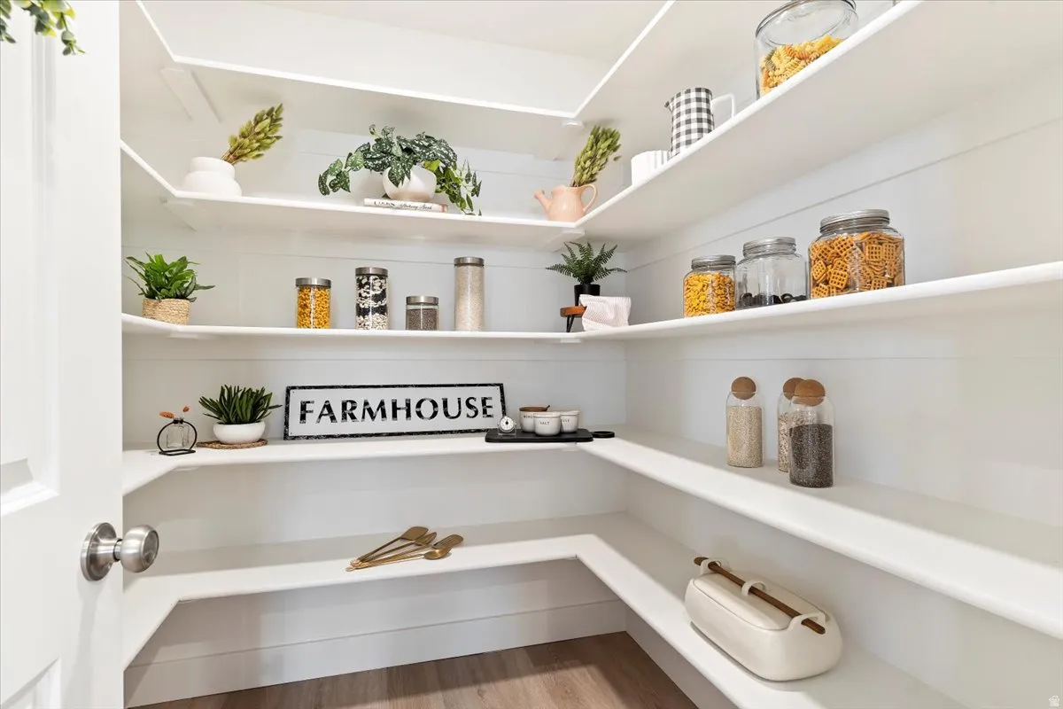 Walk-in pantry featuring extensive white shelving and wood-finish flooring