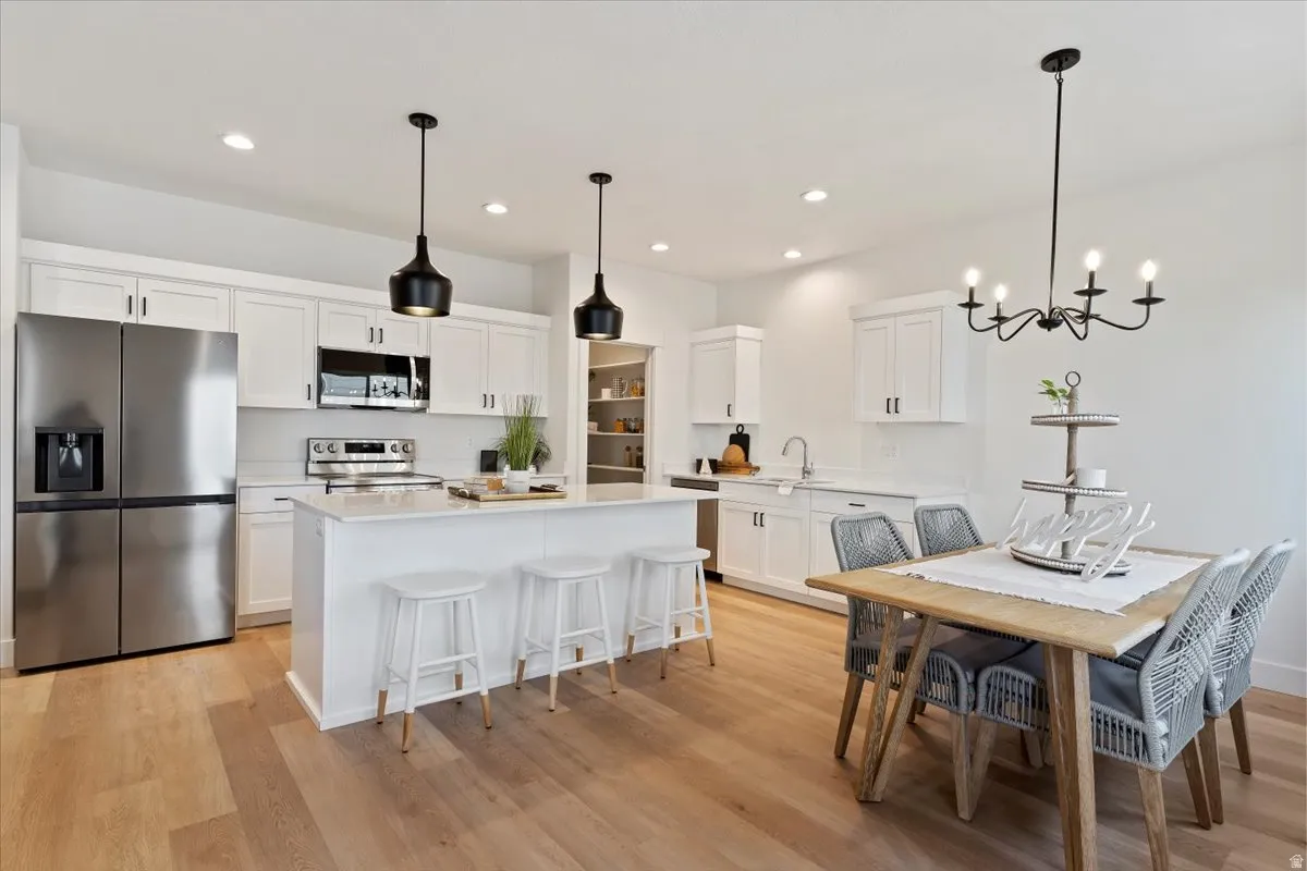 Kitchen featuring white cabinetry, stainless steel appliances, a center island with pendant lighting, and wood-finish flooring